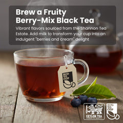 Glass mug of fruity berry-mix black tea with tea leaves and berries on a wooden surface, featuring 'Bud to Cup' branding.