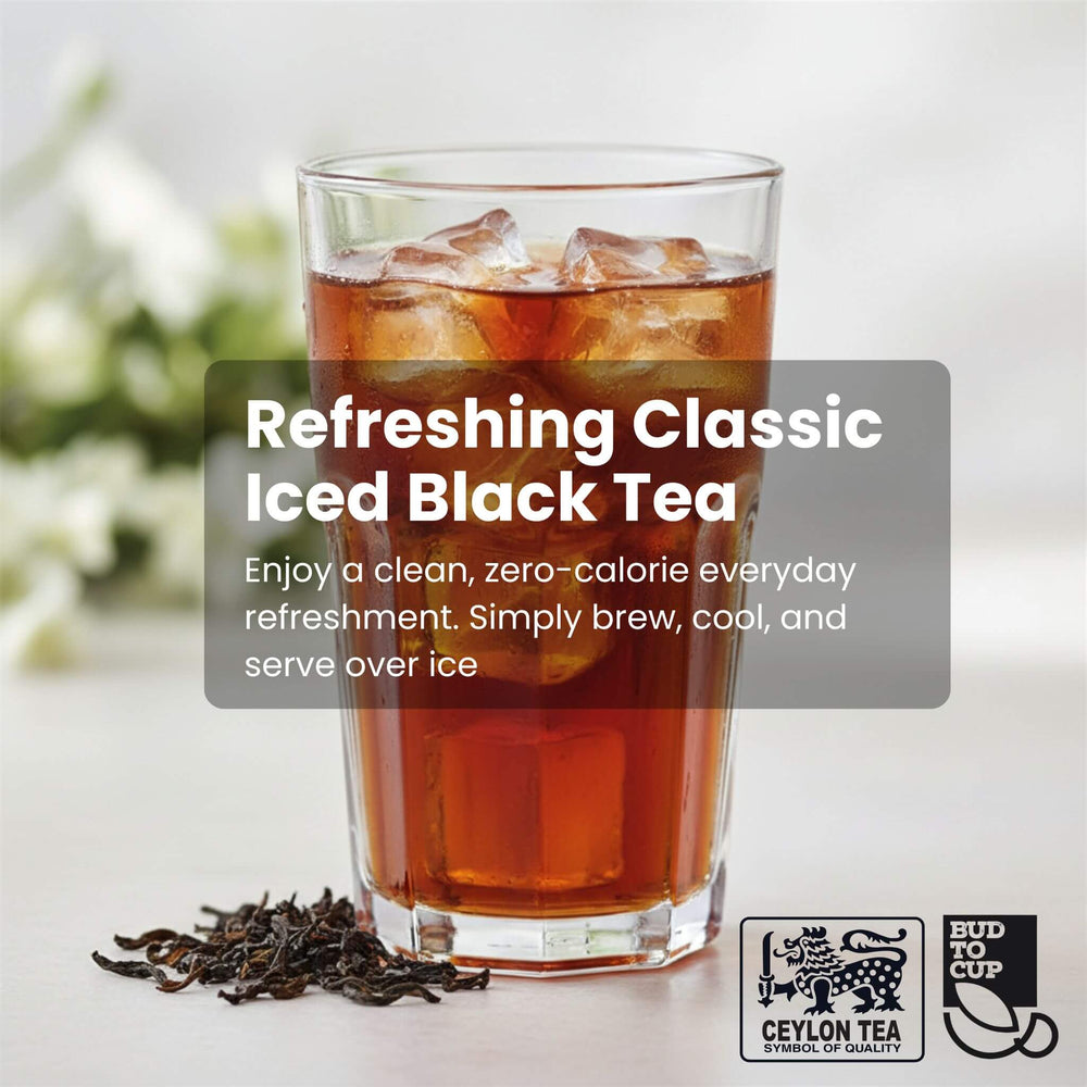Glass of iced black tea with ice cubes, surrounded by loose tea leaves on a light background.