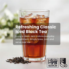 Glass of iced black tea with ice cubes, surrounded by loose tea leaves on a light background.