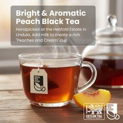 Glass of peach black tea with a teabag, peach slice, and teapot on a wooden surface.