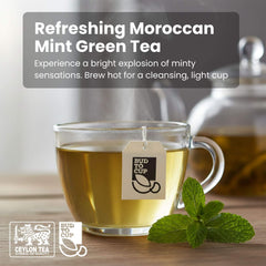 Glass of Moroccan Mint Green Tea with a tea bag label, mint leaves, and teapot in the background.